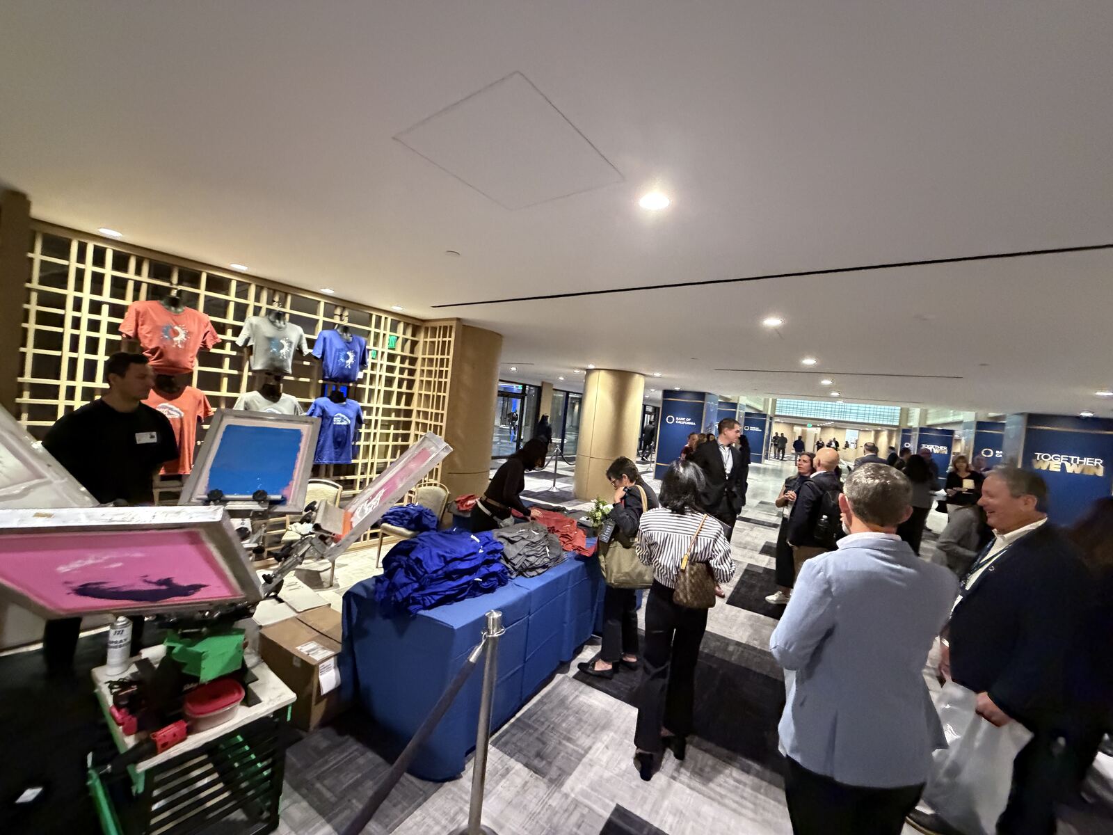 Professional booth display with branded t-shirts on yellow lit shelving and attendees browsing merchandise in corporate venue
