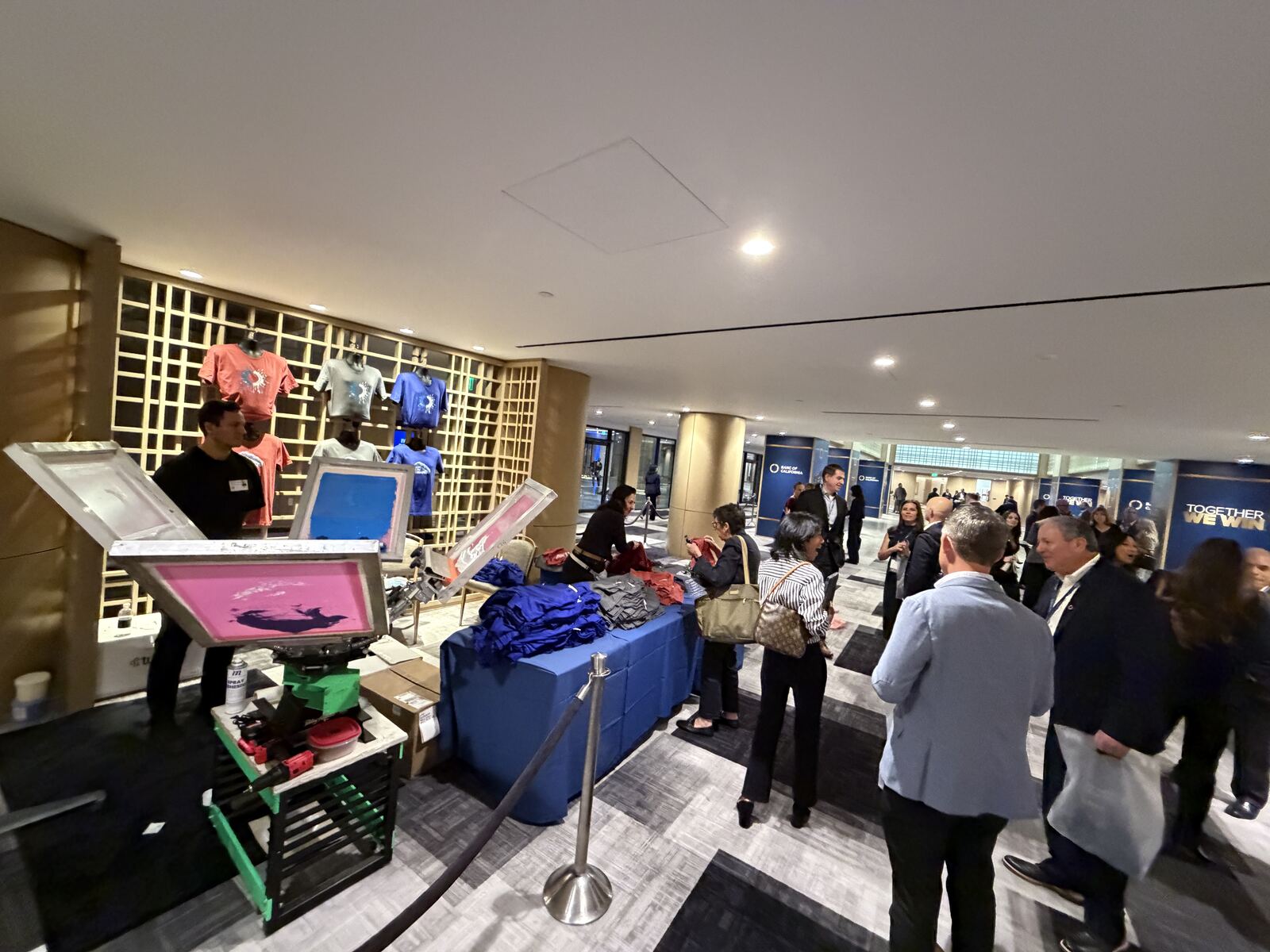 Trade show booth with illuminated product displays, colorful printed t-shirts, and multiple attendees in professional business casual attire